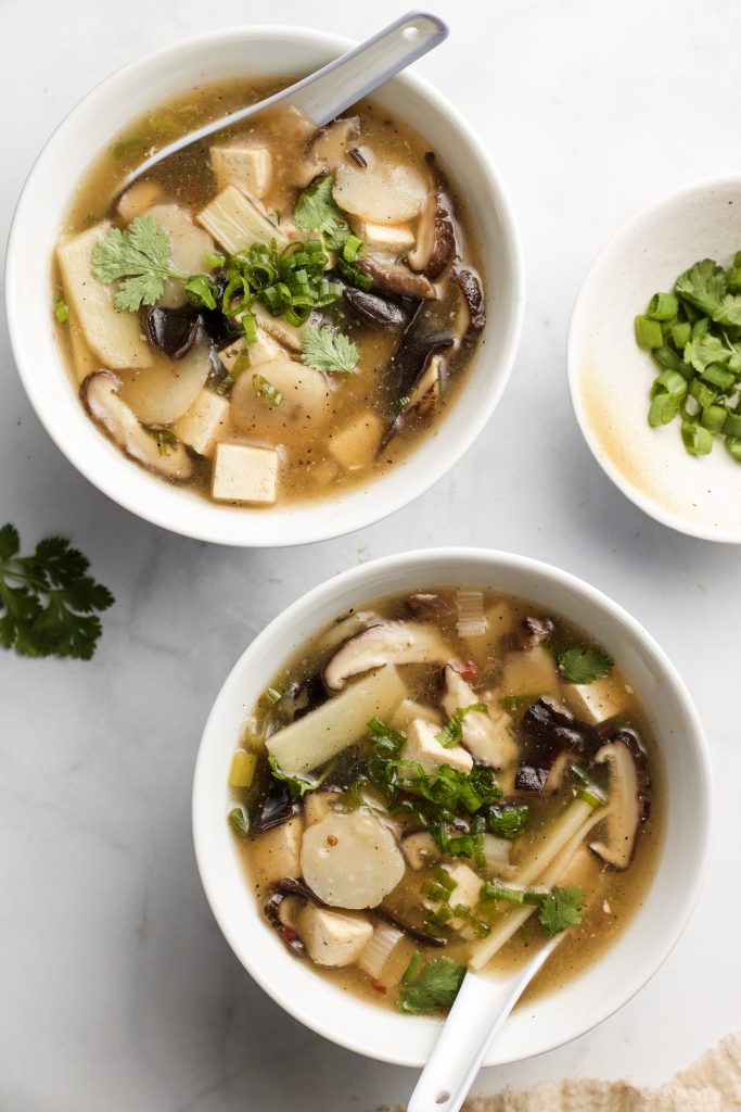 chinese sour soup in two bowls with mushrooms, bamboo, water chestnuts and scallions
