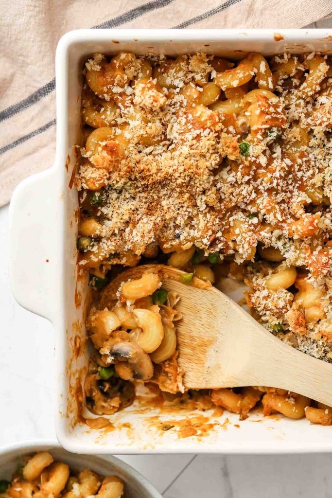 healthy tuna noodle casserole in a baking dish with breadcrumbs and a wooden spoon