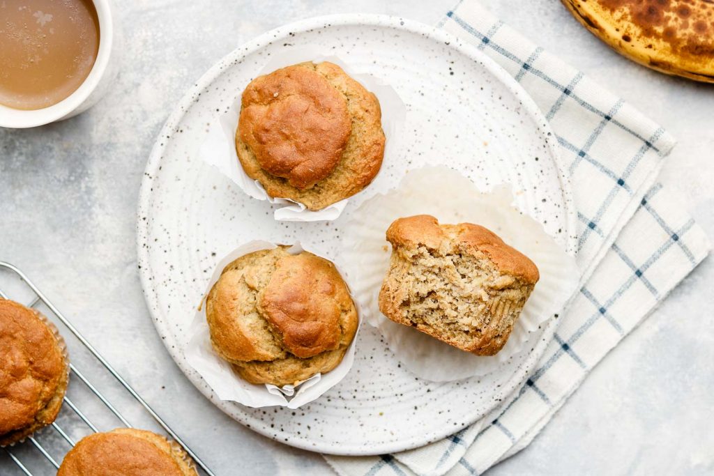 banana muffins on a speckled white plate on top of a checkered kitchen towel
