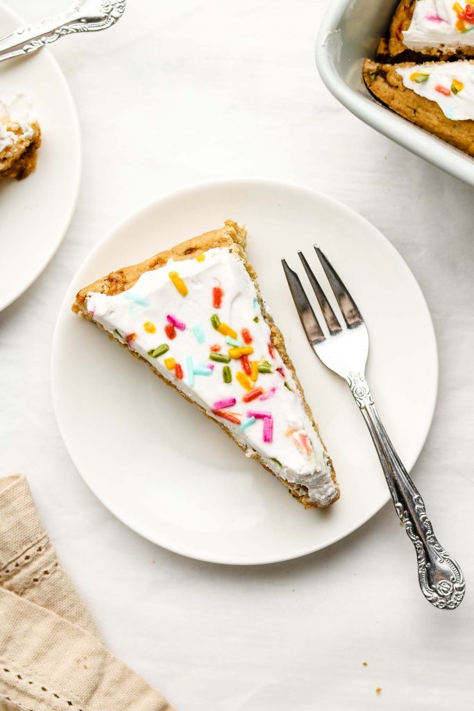 funfetti cake with vegan whip cream and sprinkles on top on a white plate and fork