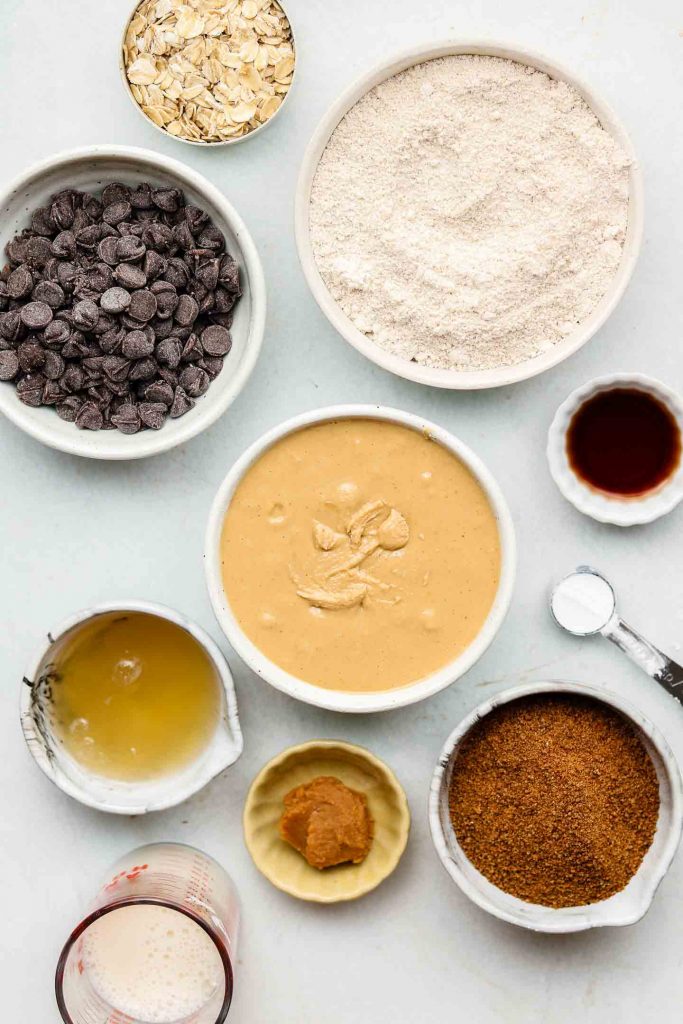 ingredients for peanut butter oatmeal cookie bars in white bowls on a blue backdrop