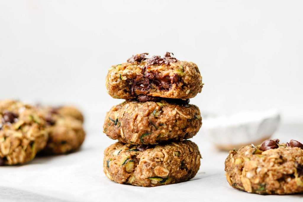stack of eggless zucchini oatmeal cookies on parchment paper with a bite taken out of the top cookie