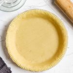 healthy pie crust made with almond flour in a glass pie dish with a rolling pin in the corner