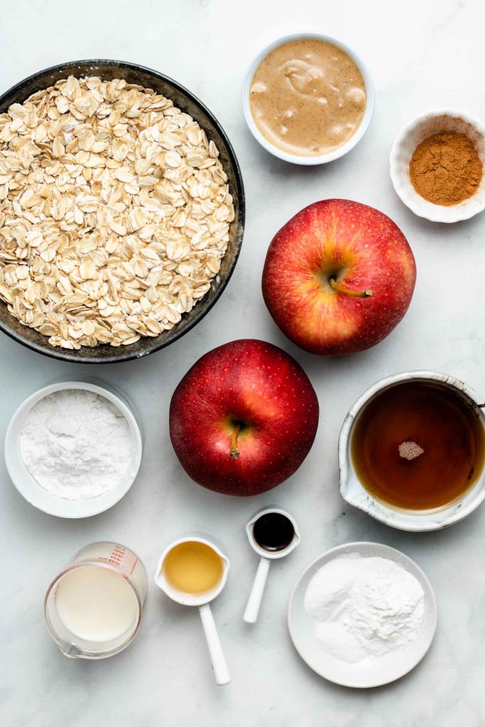 ingredients for healthy apple cinnamon muffins in bowls on a blue backdrop