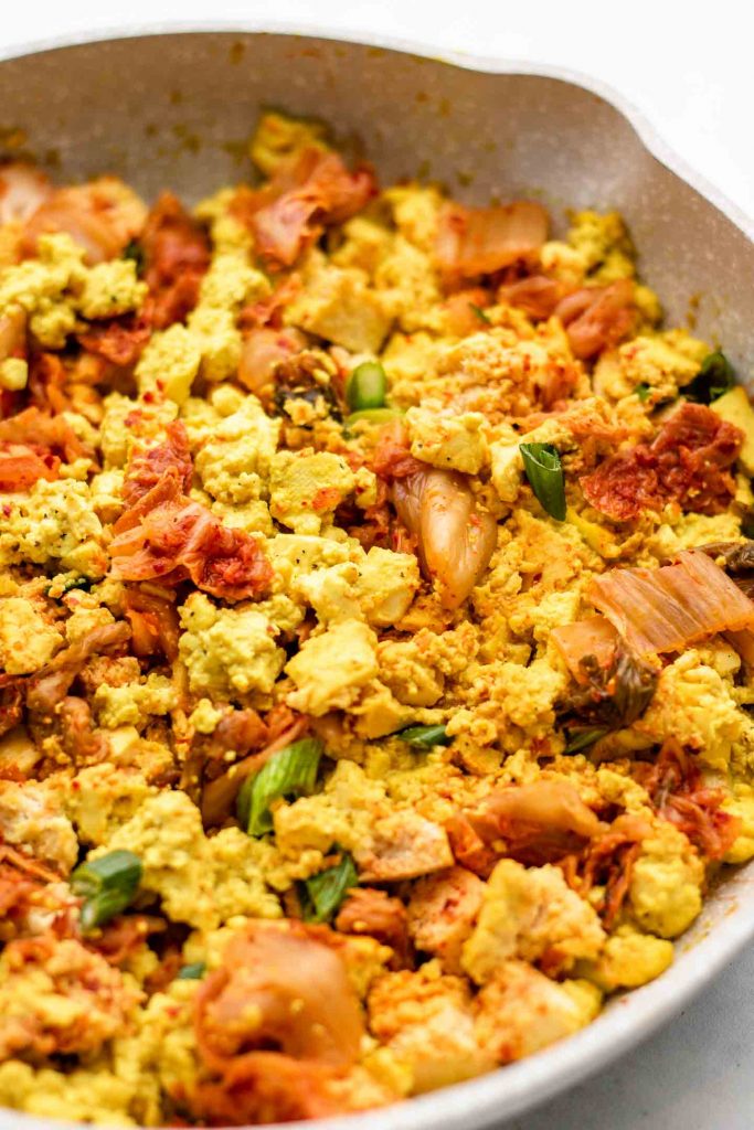 close of shot of tofu scramble in a speckled pink pan with kimchi and scallions