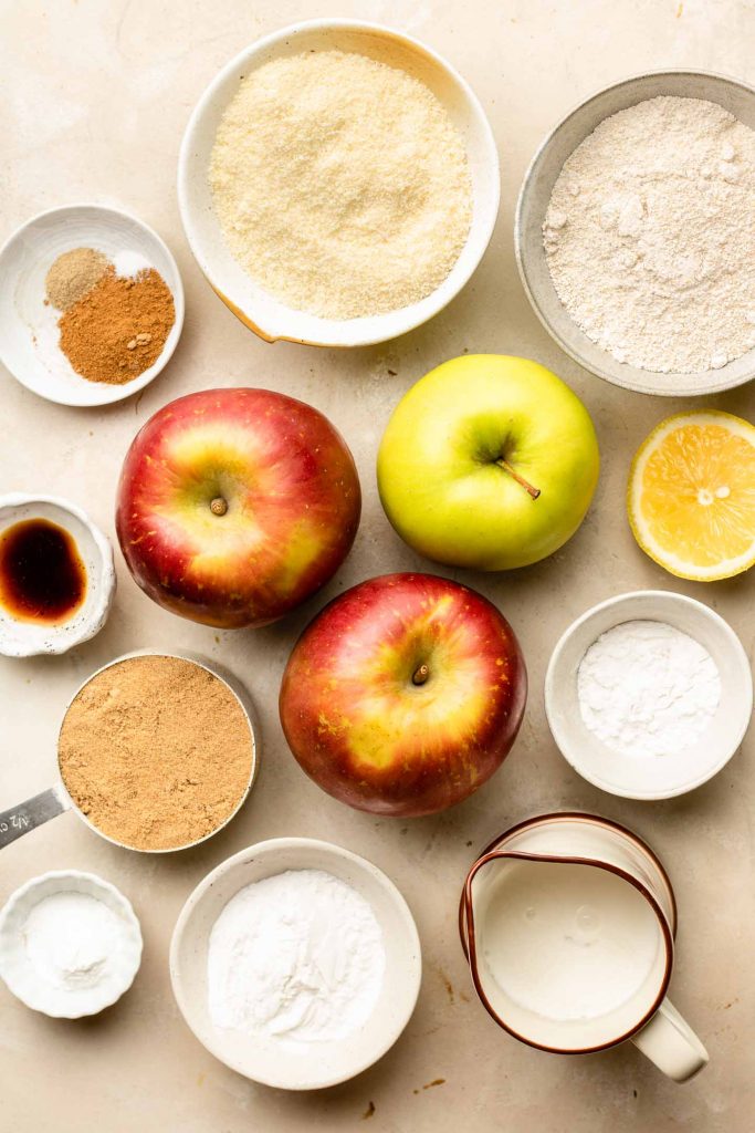 ingredients for apple cobbler in small bowls on a beige backdrop