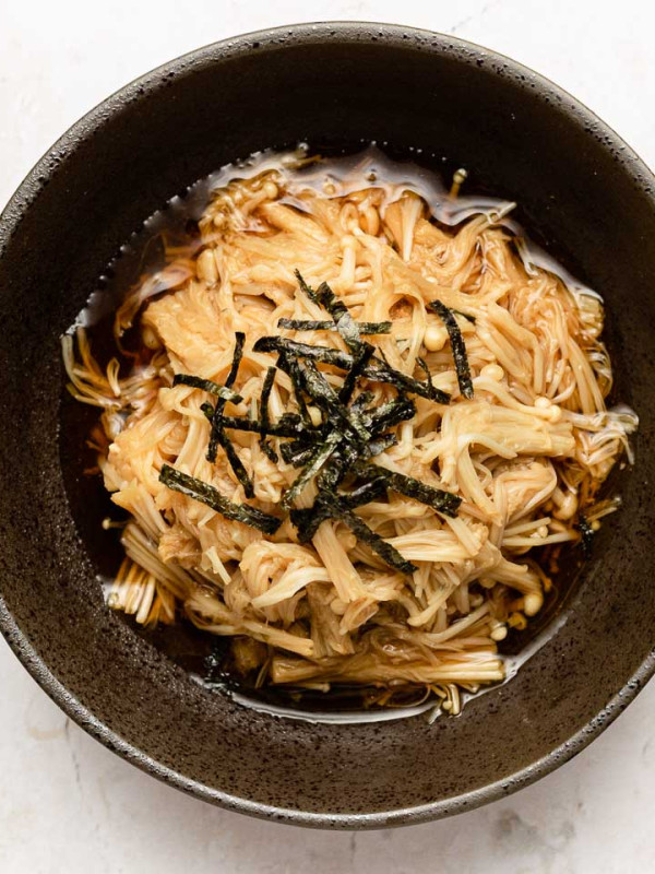 cooked enoki in a black bowl with soy butter sauce and nori on top
