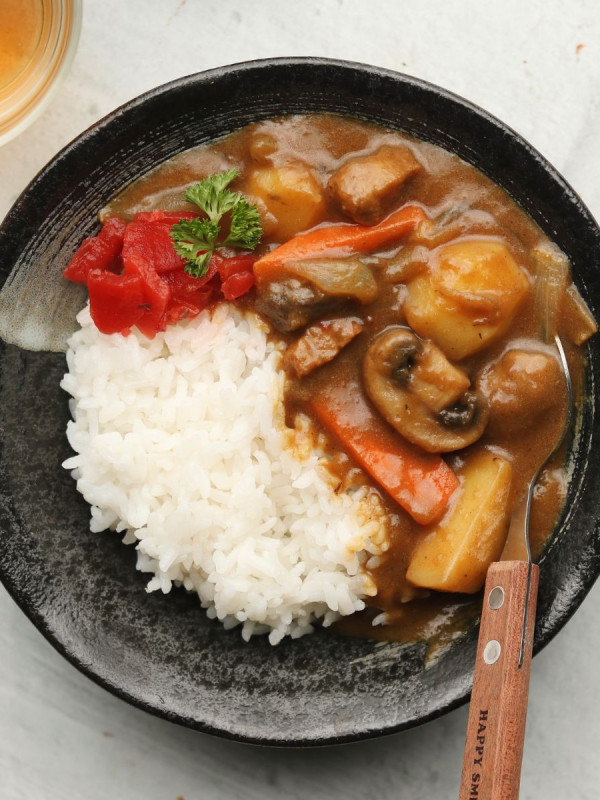 Japanese curry in a black bowl with rice, pickles and a brown spoon